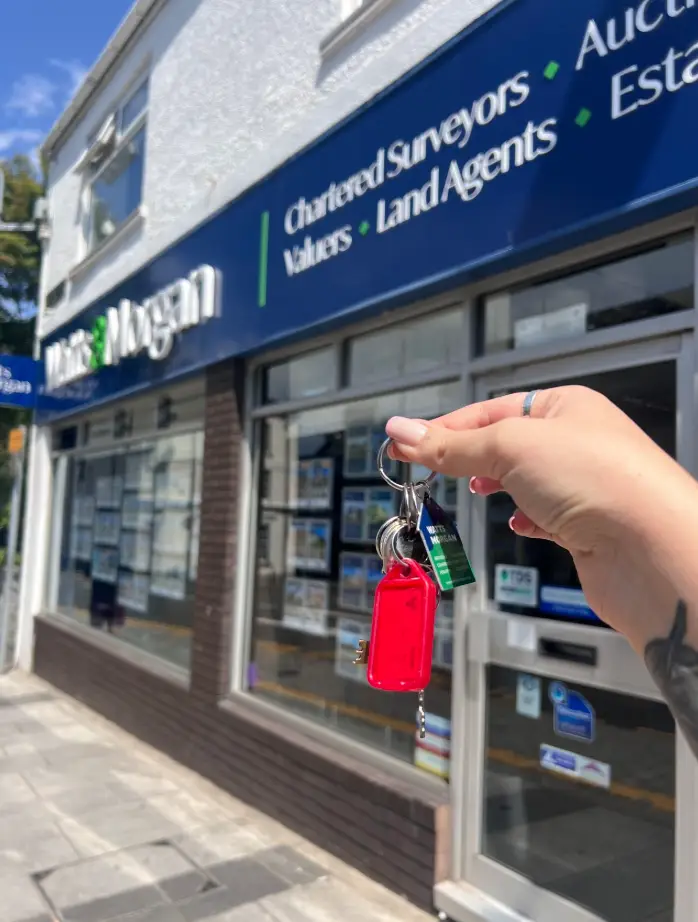 Hand holding house keys outside an estate agent.